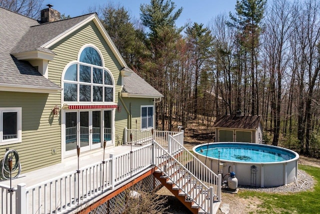 outdoor pool featuring a storage unit, an outdoor structure, a wooden deck, and stairs