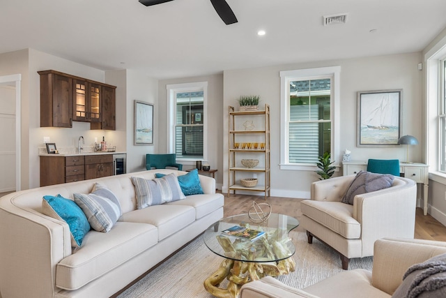 living room with beverage cooler, visible vents, light wood finished floors, indoor wet bar, and a ceiling fan