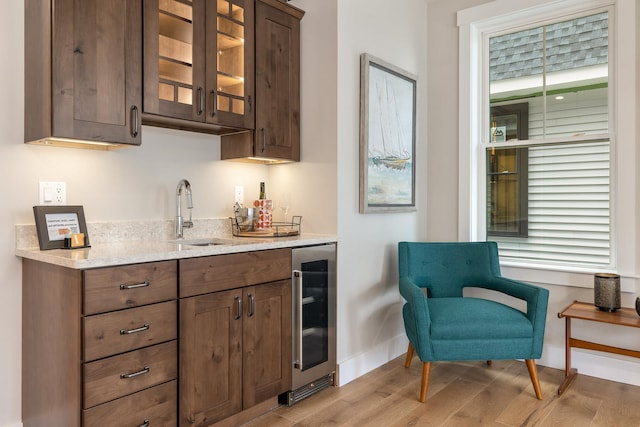 bar featuring baseboards, a sink, wet bar, light wood-type flooring, and wine cooler