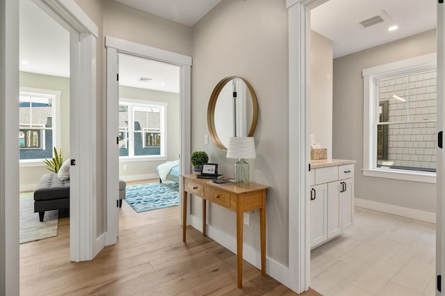 hallway featuring baseboards, visible vents, a healthy amount of sunlight, and light wood-style flooring