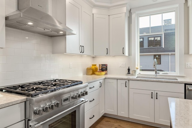 kitchen featuring a sink, backsplash, white cabinetry, wall chimney range hood, and stainless steel stove