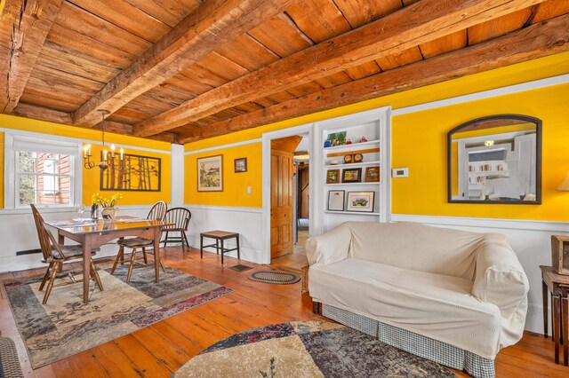 living area with beamed ceiling, a notable chandelier, wood ceiling, wainscoting, and hardwood / wood-style flooring