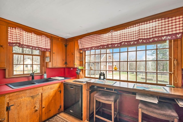 kitchen featuring black dishwasher, a sink, brown cabinets, and light countertops