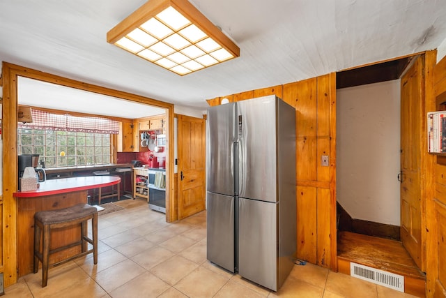 kitchen with light tile patterned floors, a breakfast bar area, visible vents, freestanding refrigerator, and brown cabinetry