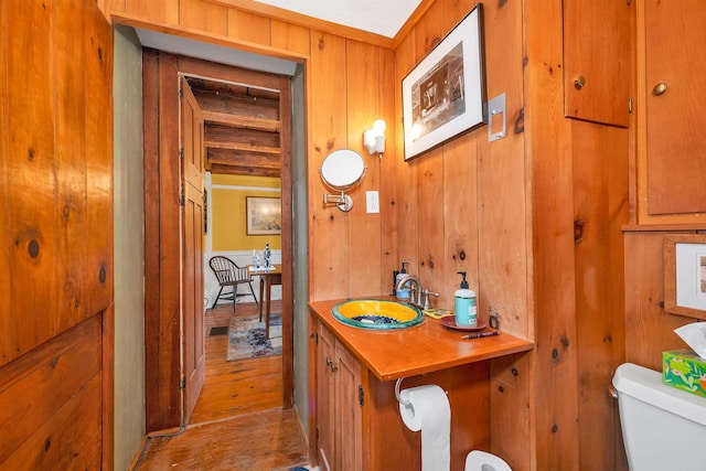 bathroom with wooden walls, wood finished floors, toilet, and a sink