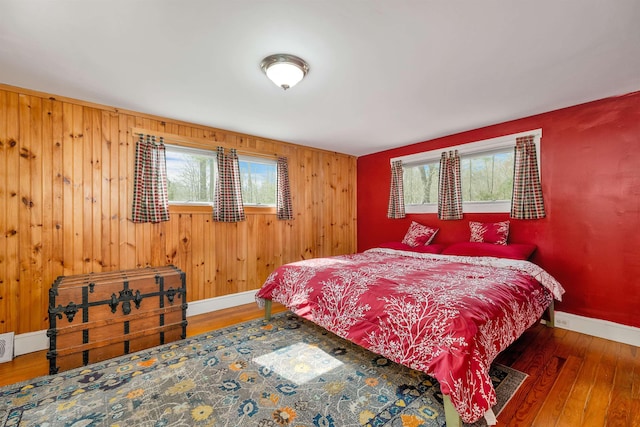 bedroom featuring wood walls, multiple windows, hardwood / wood-style floors, and baseboards