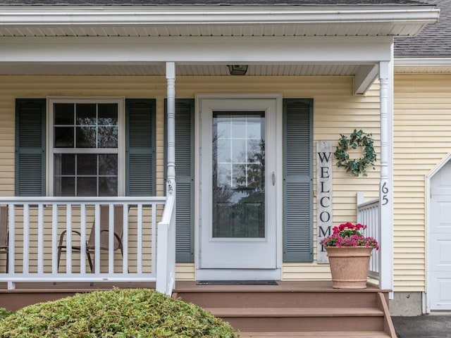 view of exterior entry featuring covered porch and roof with shingles