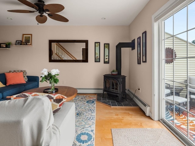 living room with ceiling fan, a baseboard radiator, a wood stove, and light wood-style flooring