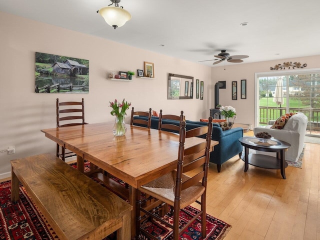 dining room with a wood stove, a ceiling fan, and light wood finished floors