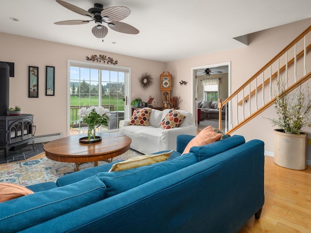 living area featuring plenty of natural light, a wood stove, stairs, and ceiling fan