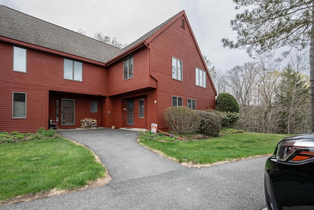 view of front facade featuring driveway, a shingled roof, and a front lawn