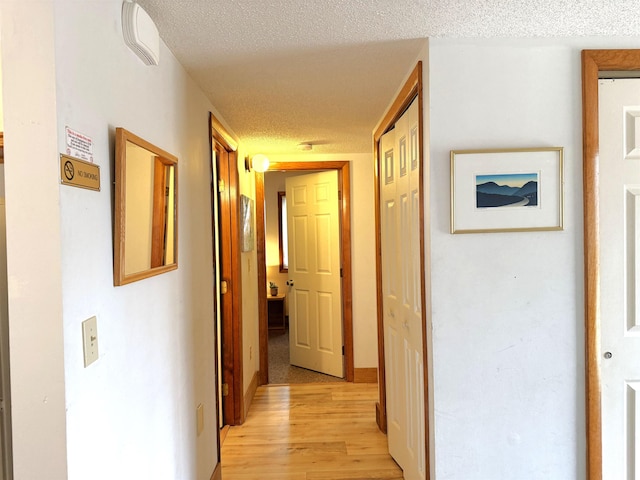 hall with a textured ceiling and light wood-style flooring