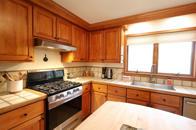 kitchen with a sink, under cabinet range hood, a wealth of natural light, tile countertops, and appliances with stainless steel finishes