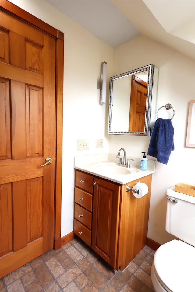 half bathroom featuring baseboards, toilet, stone finish floor, and vanity