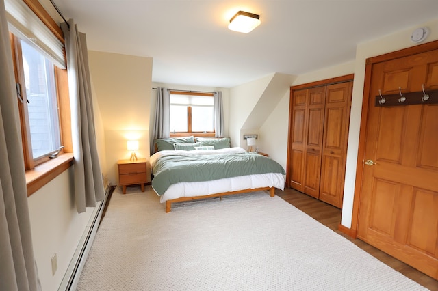 bedroom with wood finished floors, a baseboard heating unit, and a closet