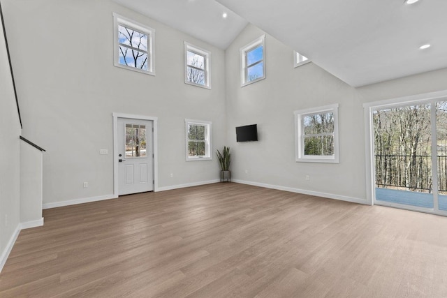 unfurnished living room with recessed lighting, high vaulted ceiling, baseboards, and light wood-type flooring