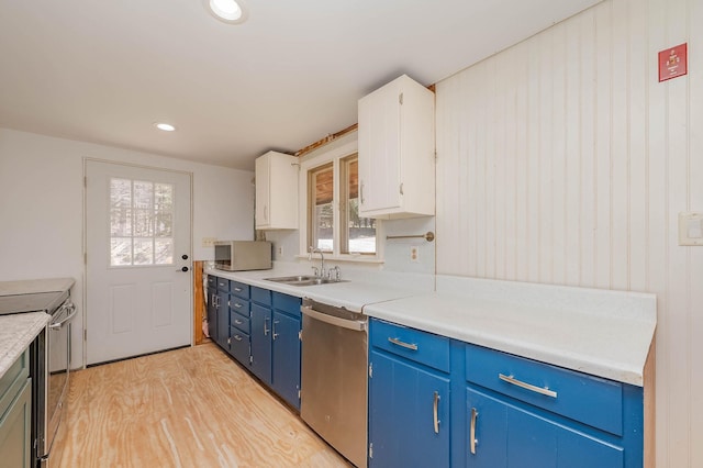 kitchen featuring blue cabinetry, stainless steel appliances, light countertops, light wood finished floors, and a sink