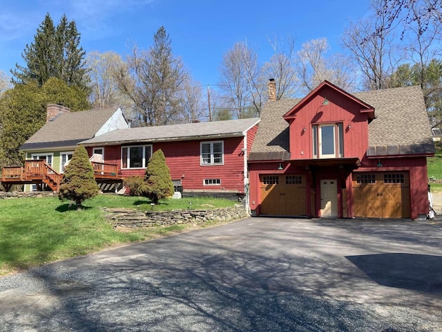 view of front of property featuring a chimney, aphalt driveway, a wooden deck, and a front yard