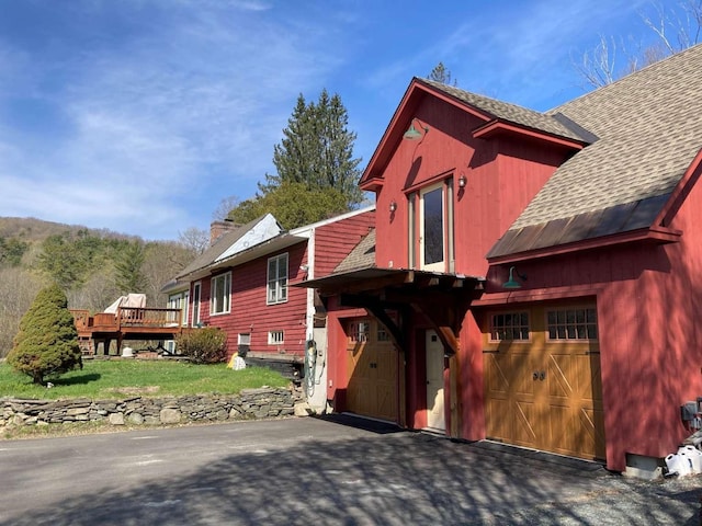 view of side of home featuring driveway, a deck, a shingled roof, a yard, and a garage