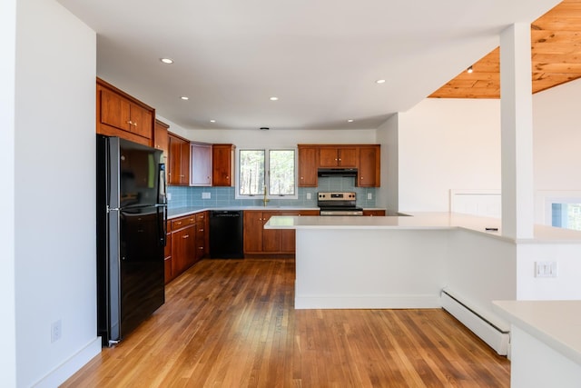 kitchen featuring under cabinet range hood, black appliances, light countertops, wood finished floors, and a baseboard radiator