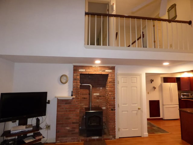 living room with a wood stove, light wood-style floors, and a towering ceiling