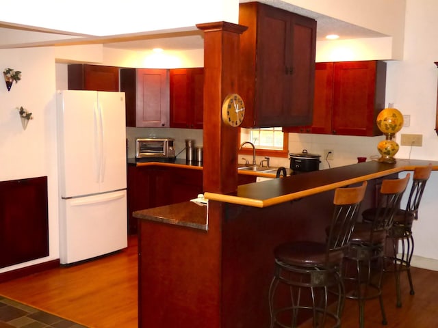 kitchen featuring reddish brown cabinets, freestanding refrigerator, a breakfast bar, a peninsula, and dark wood-type flooring