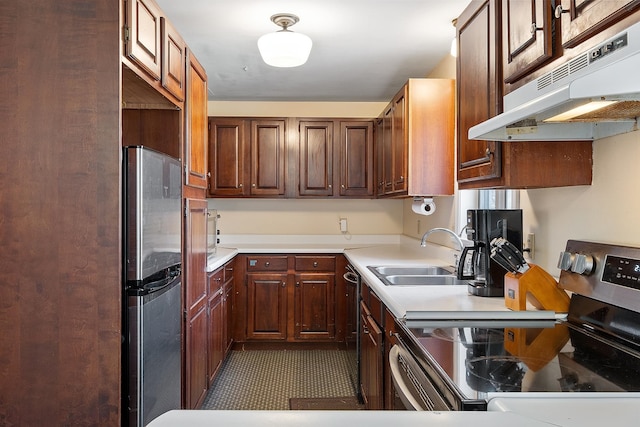 kitchen with dark tile patterned flooring, under cabinet range hood, appliances with stainless steel finishes, light countertops, and a sink