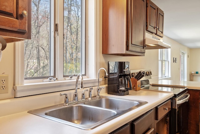 kitchen with a sink, under cabinet range hood, brown cabinetry, light countertops, and electric range