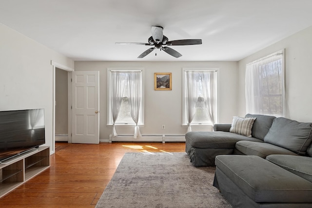 living area featuring a baseboard heating unit, ceiling fan, wood finished floors, and a healthy amount of sunlight