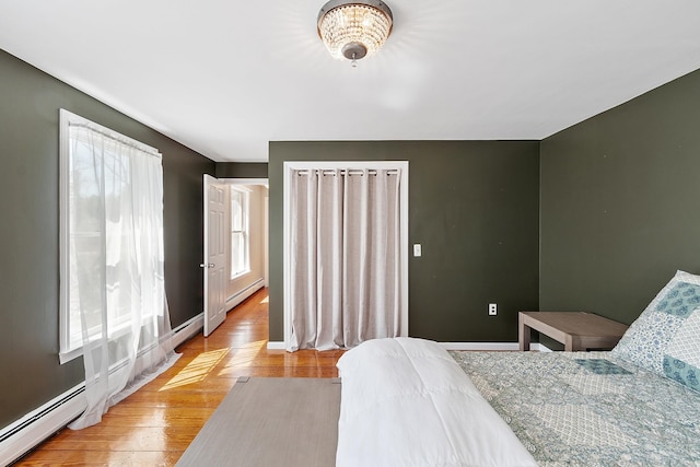 bedroom with baseboards, light wood finished floors, and a baseboard radiator