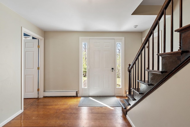 foyer entrance featuring wood-type flooring, baseboard heating, stairway, and baseboards