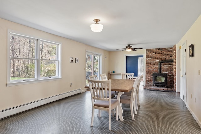 dining space featuring a baseboard heating unit, a wood stove, a ceiling fan, and baseboards