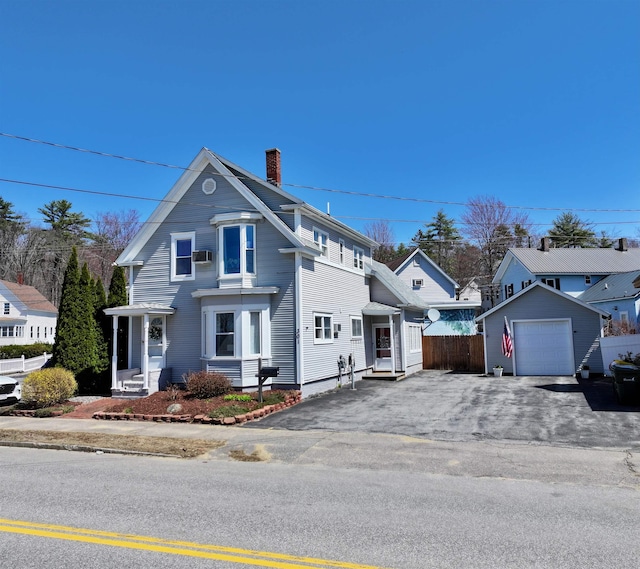 view of front of house with aphalt driveway, fence, a chimney, an outbuilding, and a detached garage