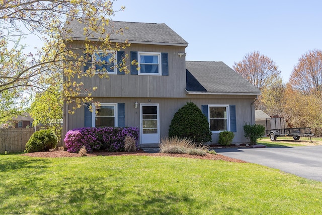 view of front of home with fence, a shingled roof, and a front yard
