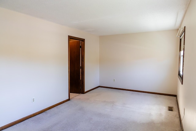 empty room featuring visible vents, baseboards, and light carpet