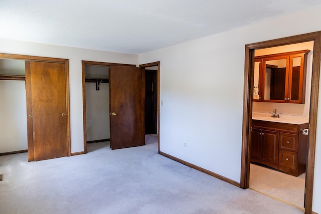 unfurnished bedroom featuring connected bathroom, light carpet, a sink, multiple closets, and baseboards