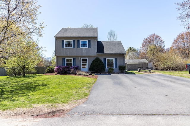colonial house with a shingled roof, aphalt driveway, fence, and a front yard