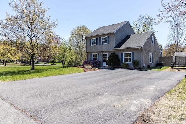 colonial inspired home with central air condition unit, fence, roof with shingles, and a front lawn