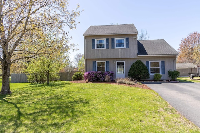 colonial inspired home with a shingled roof, a front lawn, aphalt driveway, and fence