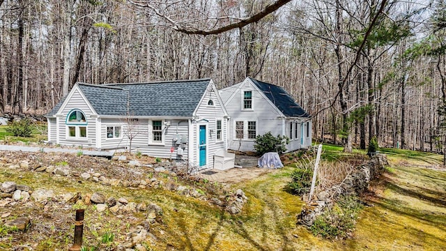 view of front of house featuring a view of trees and a shingled roof