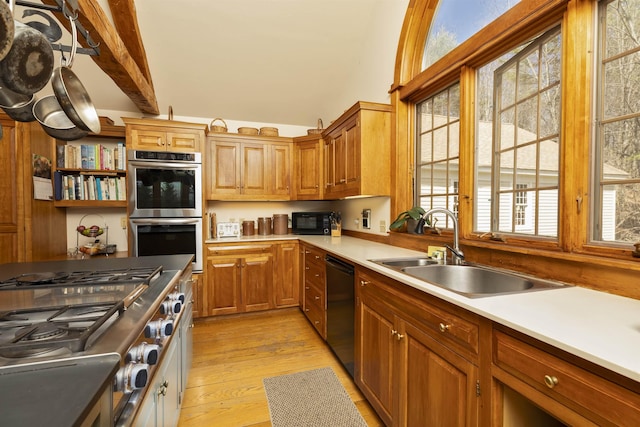 kitchen featuring brown cabinets, a sink, light wood finished floors, light countertops, and black appliances