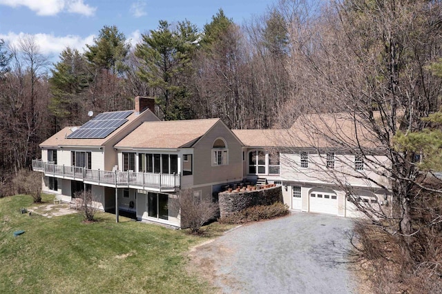 view of front of home featuring a front lawn, a wooden deck, roof mounted solar panels, a chimney, and driveway