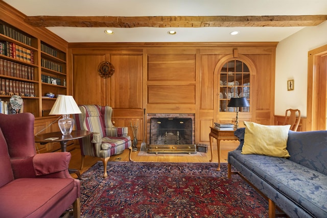 living area featuring built in shelves, a fireplace, beam ceiling, and wood finished floors