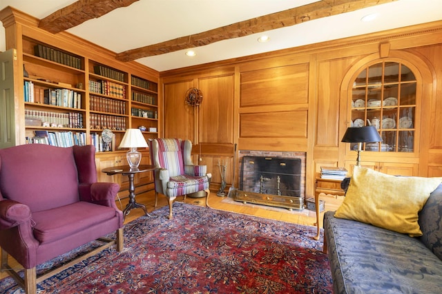 living area with wood finished floors, beam ceiling, a fireplace, recessed lighting, and built in shelves