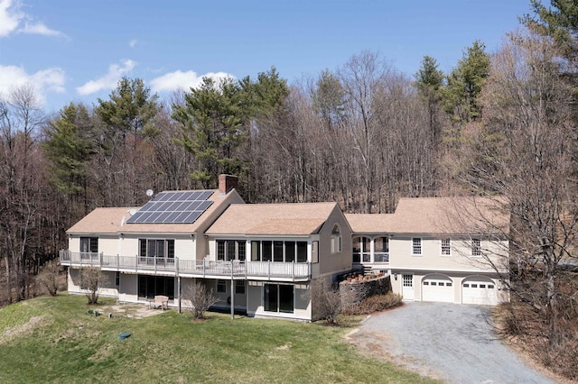 back of house featuring a chimney, a sunroom, a lawn, driveway, and solar panels