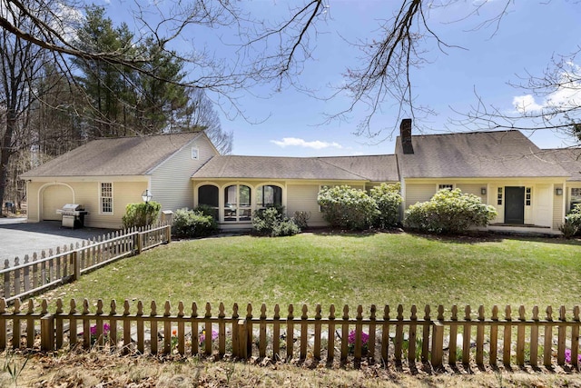view of front of house with an attached garage, a front lawn, fence private yard, a chimney, and driveway