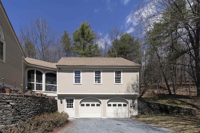 view of side of property featuring a garage, a shingled roof, and aphalt driveway