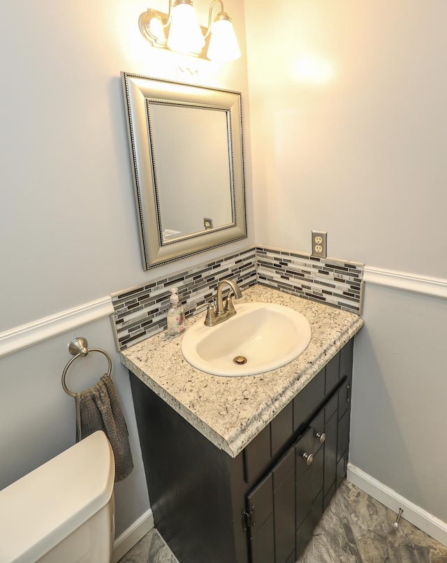 bathroom featuring toilet, baseboards, decorative backsplash, and vanity
