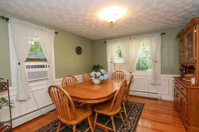 dining space with wainscoting, a healthy amount of sunlight, baseboard heating, light wood-type flooring, and a baseboard radiator