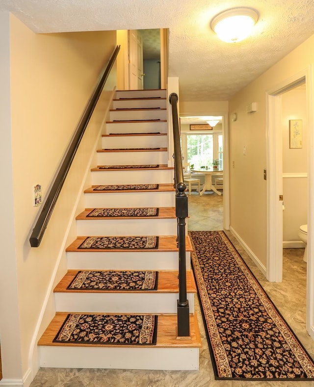 staircase with a textured ceiling and baseboards
